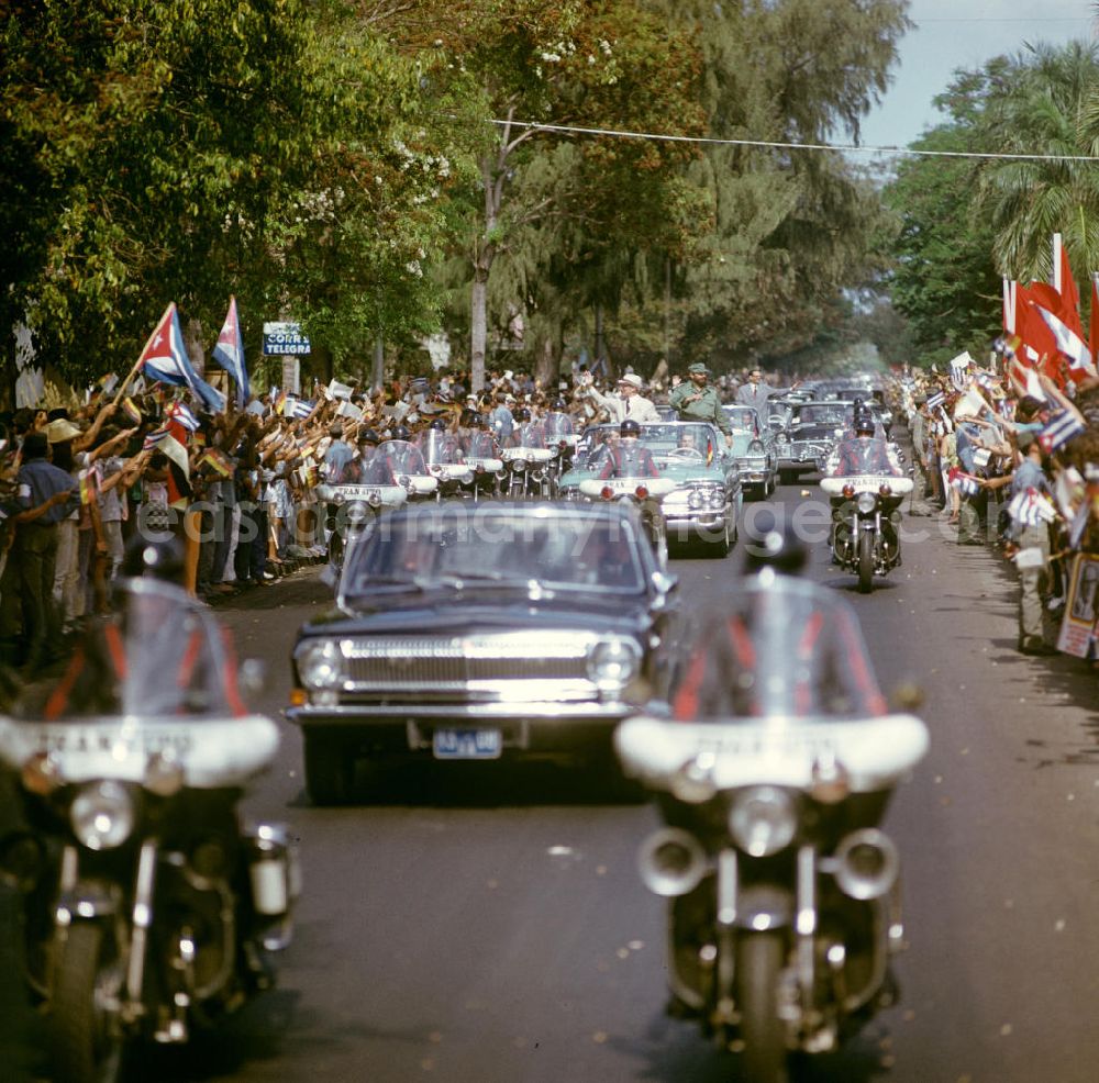 GDR picture archive: Havanna - Mit großem Jubel, DDR-Fähnchen und Willkommens-Plakaten wird in der kubanischen Bevölkerung die Ankunft des Staats- und Parteivorsitzenden der DDR, Erich Honecker, in Havanna gefeiert - hier im Wagen mit dem Regierungschef Kubas Fidel Castro. Honecker stattete vom 2