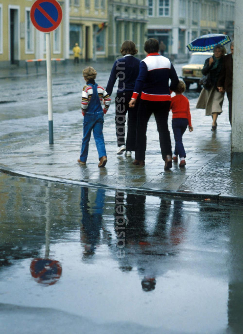 GDR photo archive: Potsdam - Straßenansicht vom Holländischen Viertel bei Regen in Potsdam. Rückansicht einer Familie mit DDR-typischer zeitgenössischer Kleidung auf dem Fußweg, daneben Schild mit Parkverbot.