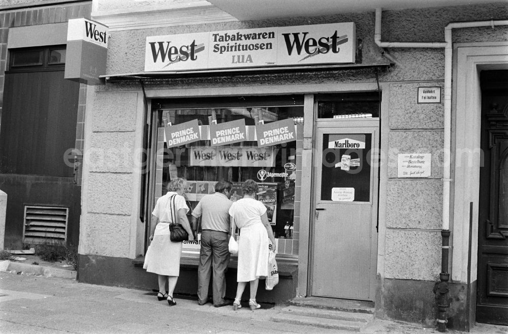 GDR picture archive: Berlin - Passers-by are standing in front of a shop for tobacco like West, Prince Denmark, Marlboro and Camel as well as spirits at the Karl-Marx-Allee in Berlin - Friedrichshain