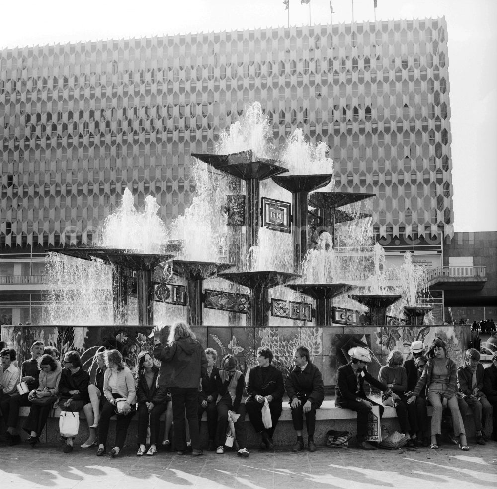 Berlin: Tourists in front of the Fountain of International Friendship in Alexanderplatz in Berlin, the former capital of the GDR, German Democratic Republic. The fountain designed Walter Womacka under the redesign of Alexanderplatz. In the background the Centrum department store Galeria Kaufhof now stands with its aluminum honeycomb facade