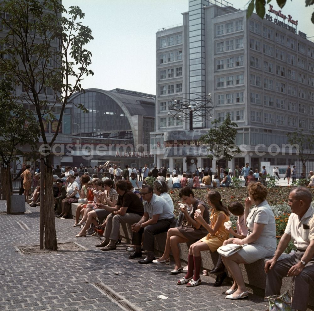Berlin - Mitte: Tourists sitting on the world clock in front of the S-train station Alexanderplatz in Berlin - Mitte. In the right background is the Berolina house to see