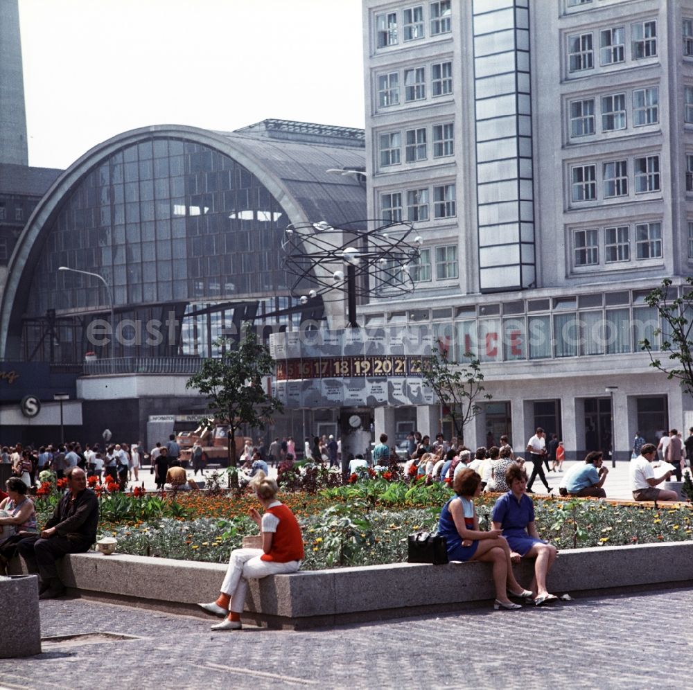 GDR image archive: Berlin - Mitte - Tourists sitting on the world clock in front of the S-train station Alexanderplatz in Berlin - Mitte. In the right background is the Berolina house to see