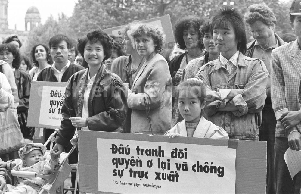 GDR photo archive: Berlin - Vietnamese guest workers - contract workers on Karl-Liebknecht-Strasse in front of the palace hotel with protest poster and banner slogan Right to stay for GDR contract workers in the Mitte district of Berlin East Berlin on the territory of the former GDR, German Democratic Republic