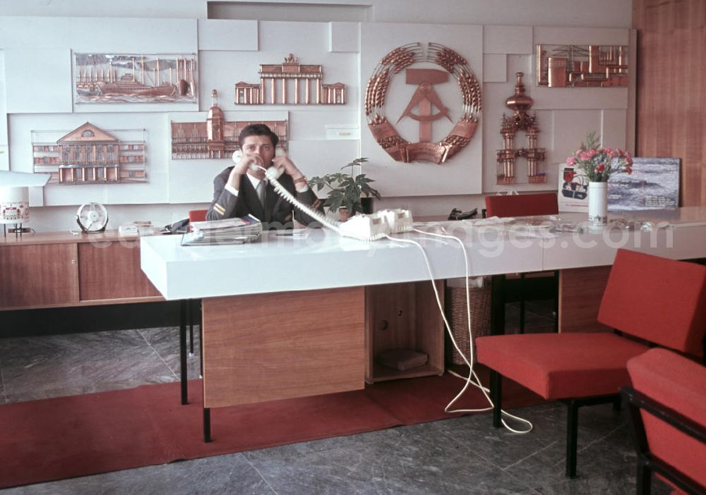 GDR picture archive: Budapest - Ein Angestellter telefoniert in der Vertretung der DDR-Fluggesellschaft Interflug in der ungarischen Hauptstadt Budapest mit zwei Telefonen gleichzeitig. Im Hintergrund die verschiedenen kulturellen Sehenswürdigkeiten der DDR.