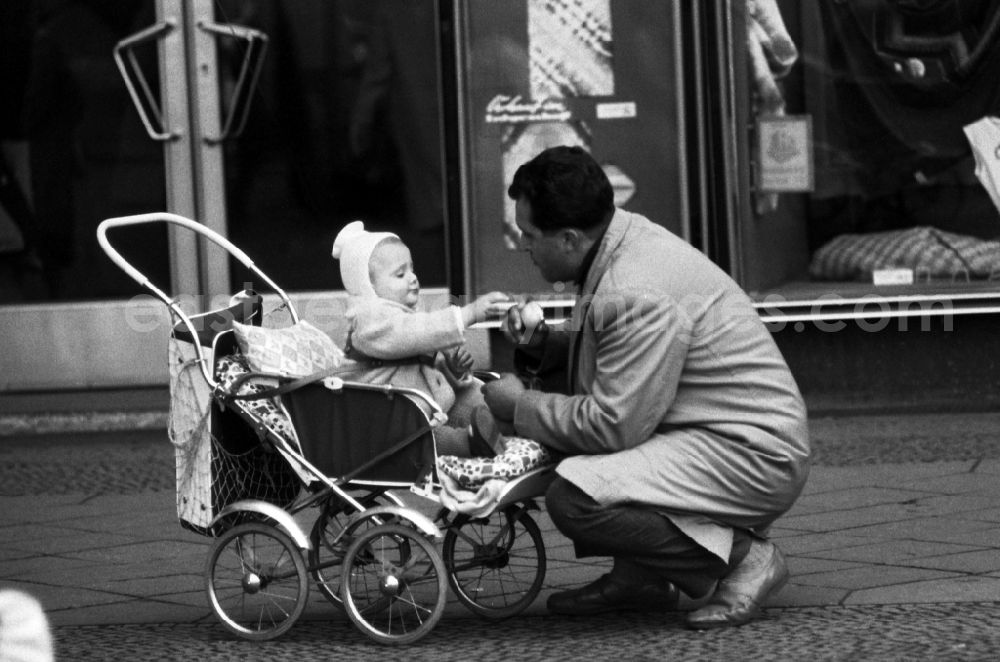 Berlin: Father kneels in front of his child sitting in a stroller in East Berlin in the territory of the former GDR, German Democratic Republic