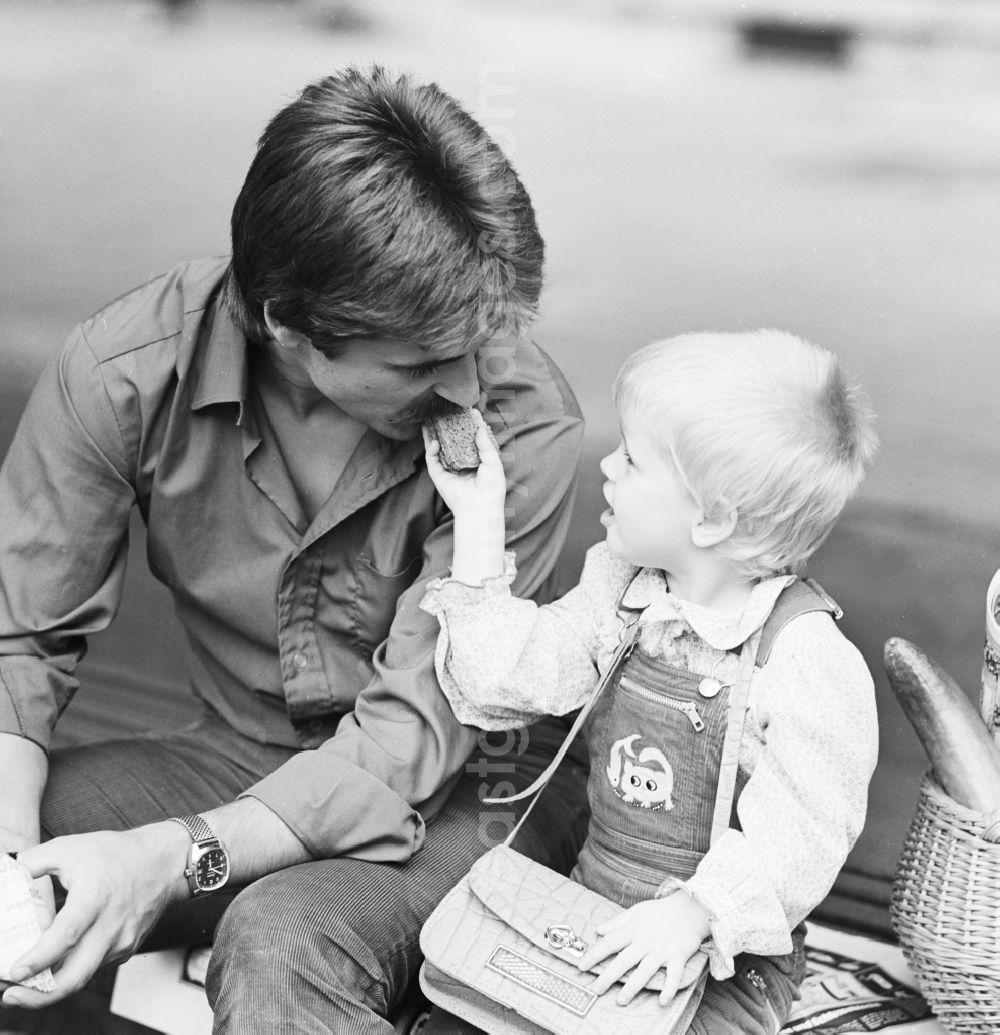 GDR picture archive: Berlin - Father sitting with his child on a bench and eat a sandwich in Berlin, the former capital of the GDR, the German Democratic Republic