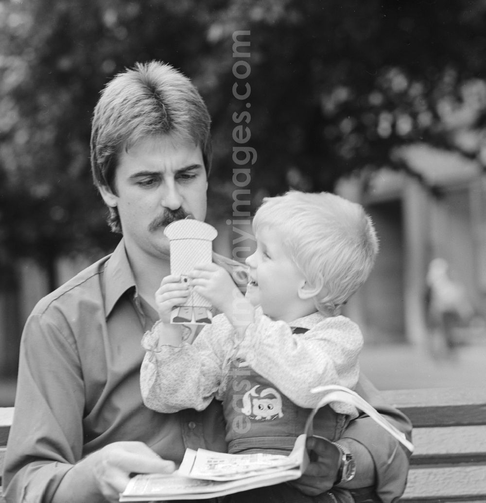 GDR photo archive: Berlin - Father sitting with his child on a bench and read a magazine in Berlin, the former capital of the GDR, the German Democratic Republic