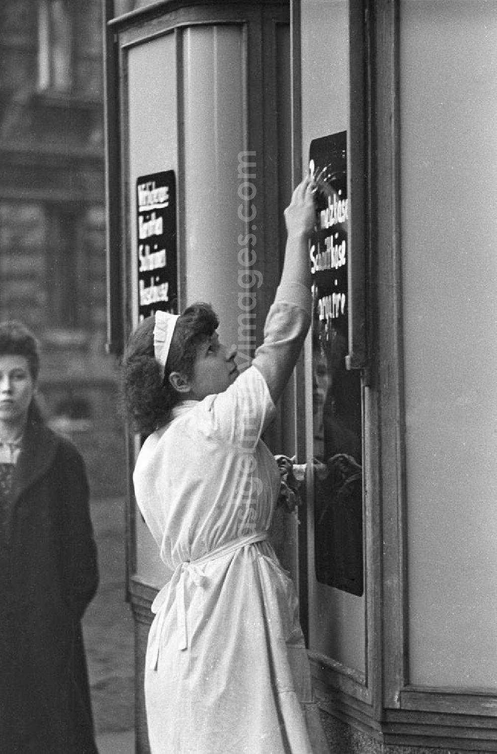 Leipzig: Eine Verkäuferin wischt eine Tafel am Eingang von einem Geschäft. Sie trägt einen weißen Kittel und eine Haube. Bestmögliche Qualität nach Vorlage!