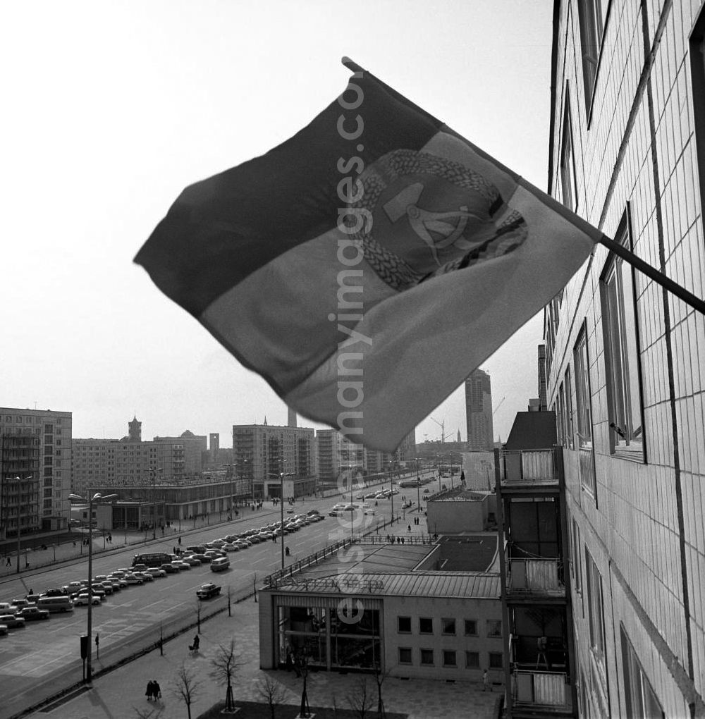 Berlin: An einem Neubaublock an der Karl-Marx-Allee, der Pracht- und Paradestraße von Berlin (Ost), weht eine Fahne mit DDR-Enblem am Fenster einer privaten Wohung. Die Menschen, die hier zu DDR-Zeiten mit Blick auf den Alexanderplatz (Hintergrund) wohnten, gehörten zur privilegierten Schicht bzw. waren angesehene Arbeiter. An den Feiertagen, wie 1. Mai oder 7.Oktober, wurde unten auf der achtspurigen Straße die Tribüne für die Partei- und Staatsführung aufgebaut, auf der die Politiker dann huldvoll die vorbeiziehenden Werktätigen begrüßten.