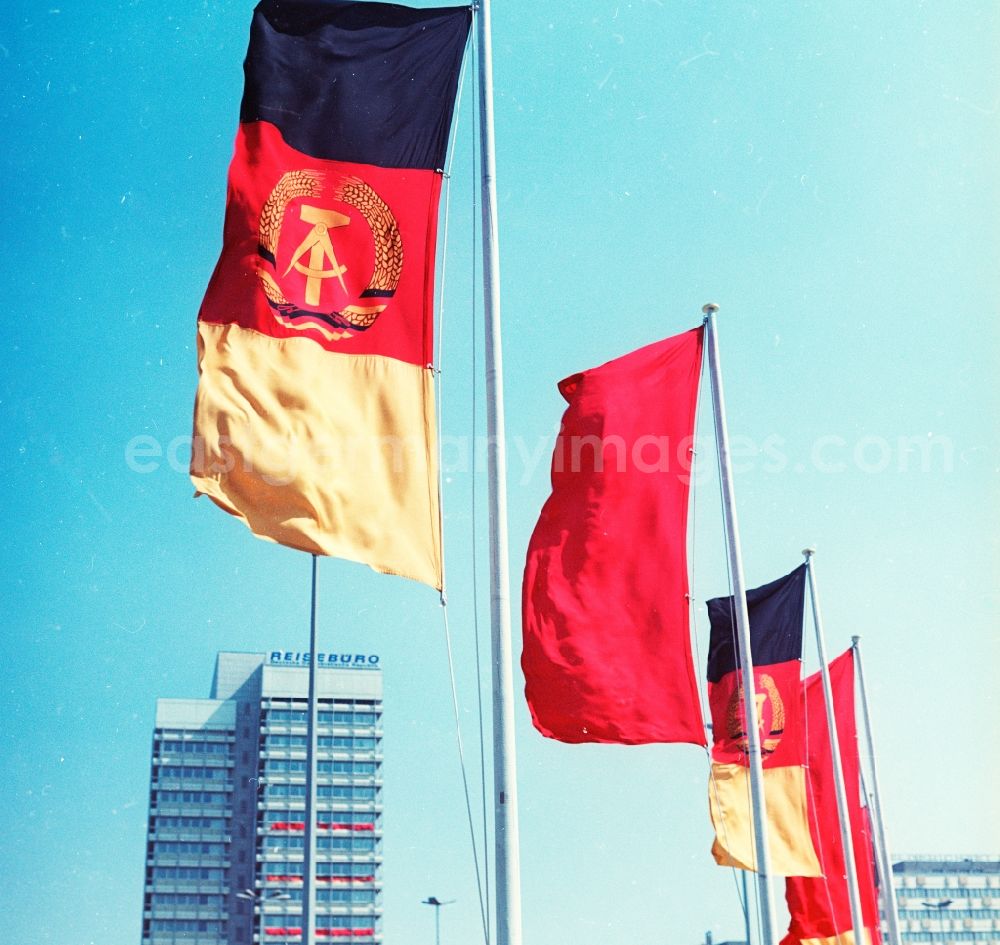 GDR picture archive: Berlin - Waving flags of the GDR and the working class in Berlin. The flag of the German Democratic Republic was the color of the Weimar Republic. On the colors black, red and gold is in the middle the coat of arms of the GDR with hammer, compasses and wreath of grain ears. The red flag was designated in the GDR as a laborer flag