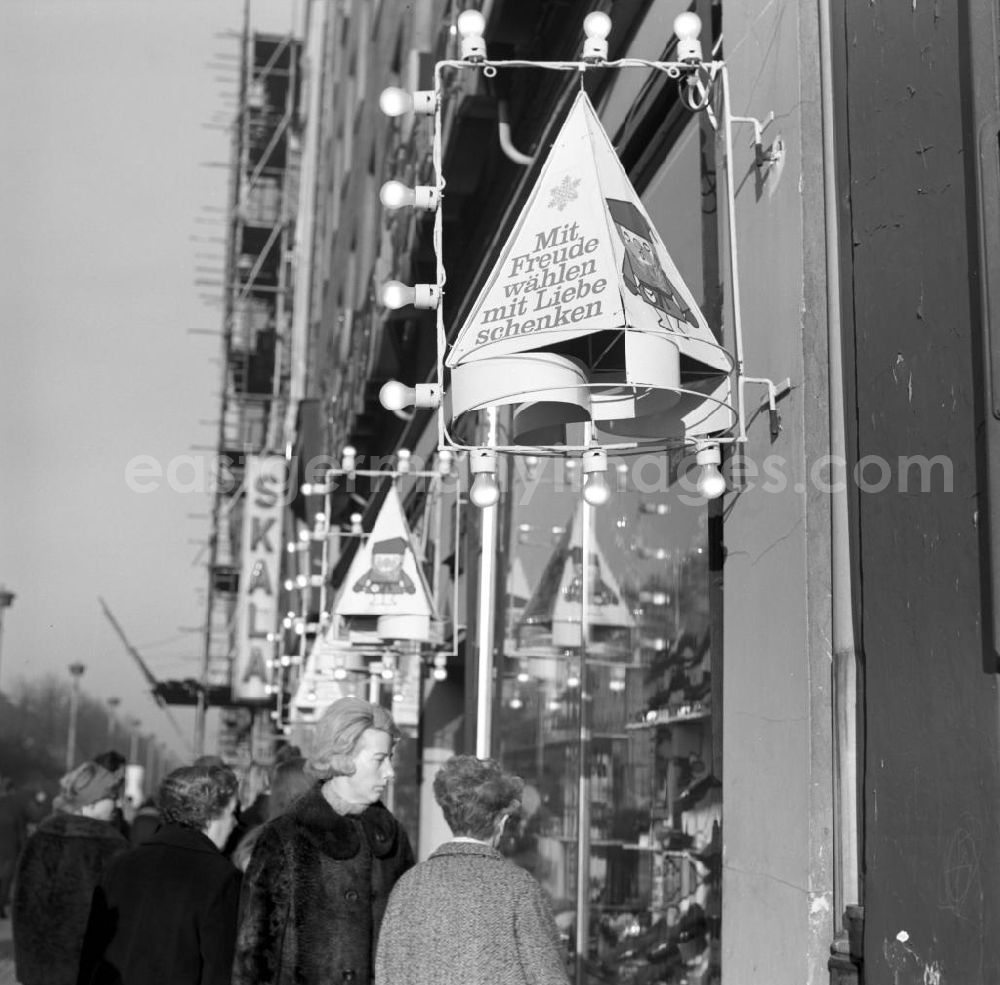 GDR image archive: Berlin - Festlich geschmückt lädt das Schuhgeschäft Hans Sachs in der Schönhauser Allee in Berlin mit dem Slogan Mit Freude wählen, mit Liebe schenken zum Weihnachtsbummel ein. Im Hintergrund die Leuchtreklame des Kino Skala.