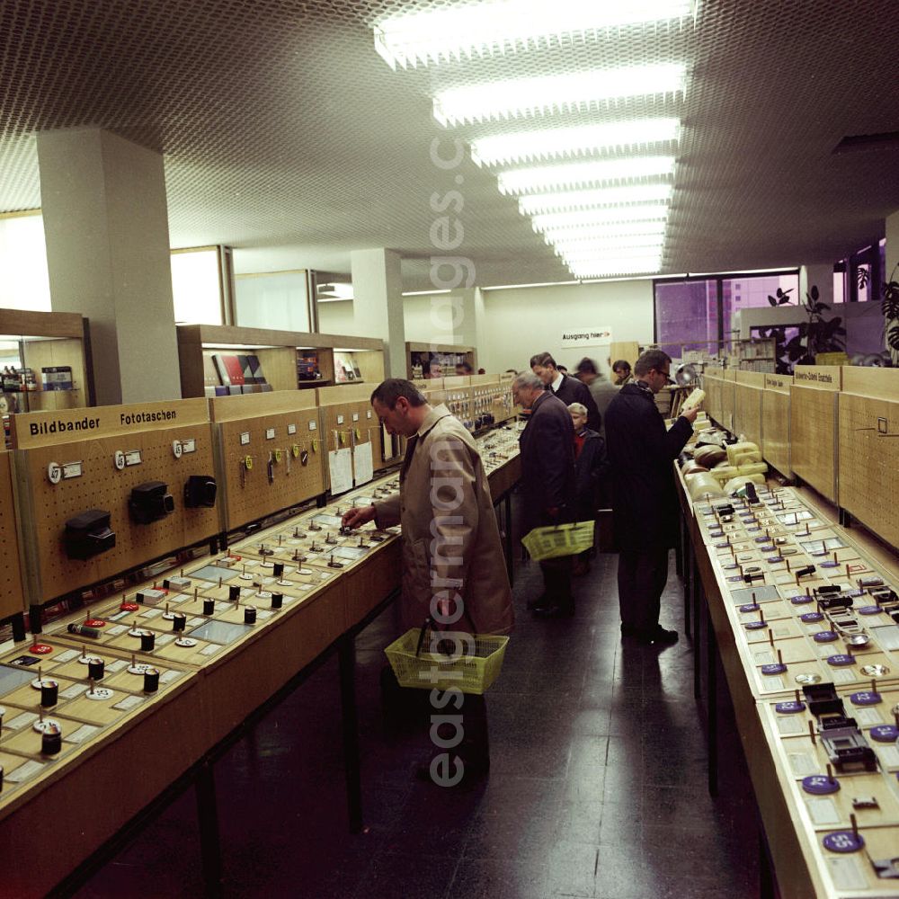 GDR photo archive: Berlin - Kunden beim Einkauf in einer Regalreihe mit Foto - Zubehör in einem Carl Zeiss Jena Fachgeschäft am Alexanderplatz in Berlin Mitte.