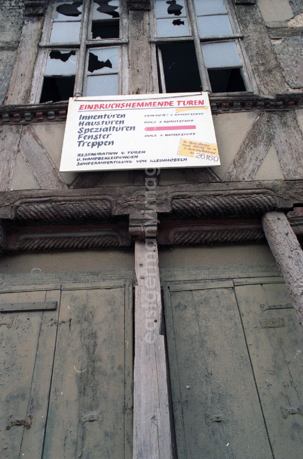 Halberstadt: Werbeschild über einer Haustür eines stark sanierungsbedürftigen Fachwerkhaus, mit der Aufschrift Einbruchshemmende Türen ..., darüber Fenster mit zerbrochenen / kaputten Fensterscheiben.