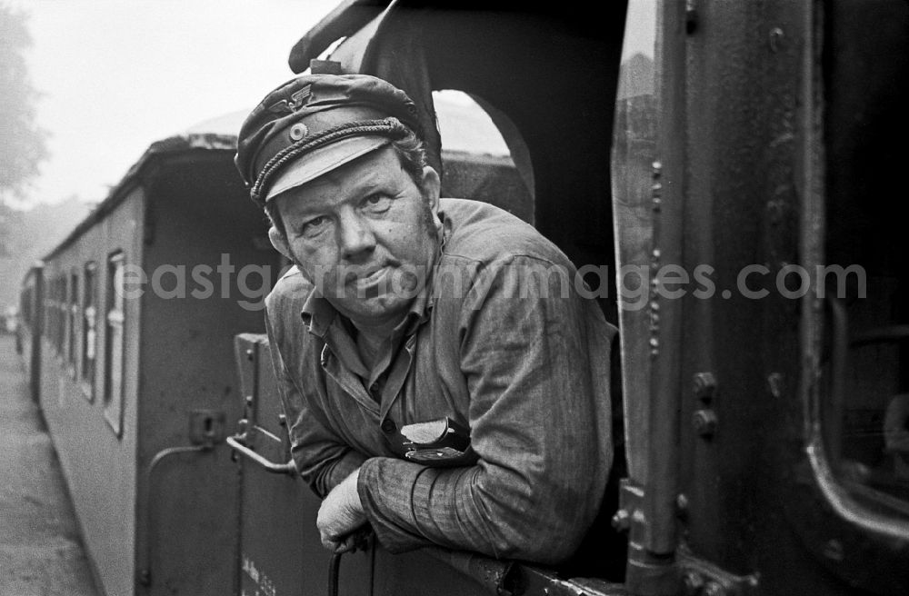 GDR picture archive: Putbus - Engine driver in the driver's cab of the train on the station grounds of the Deutsche Reichsbahn narrow-gauge railway in Putbus, Mecklenburg-Western Pomerania in the territory of the former GDR, German Democratic Republic