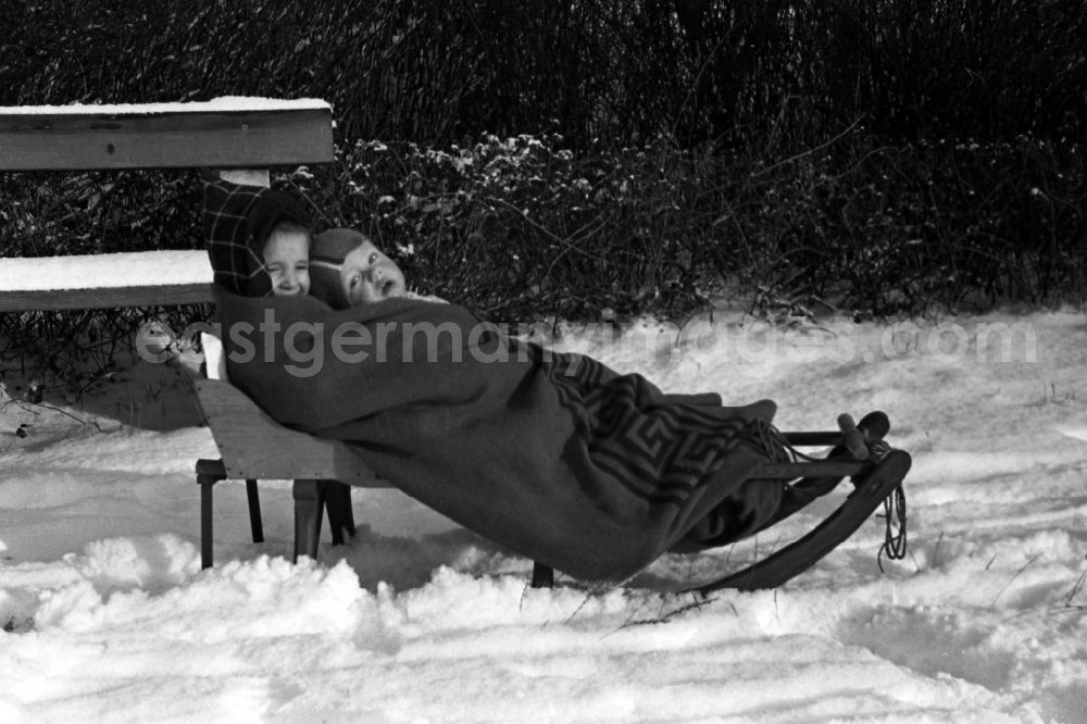 GDR photo archive: Merseburg - Two children lie, muffled in a thick cover, on a sledge in Merseburg in the federal state Saxony-Anhalt in Germany