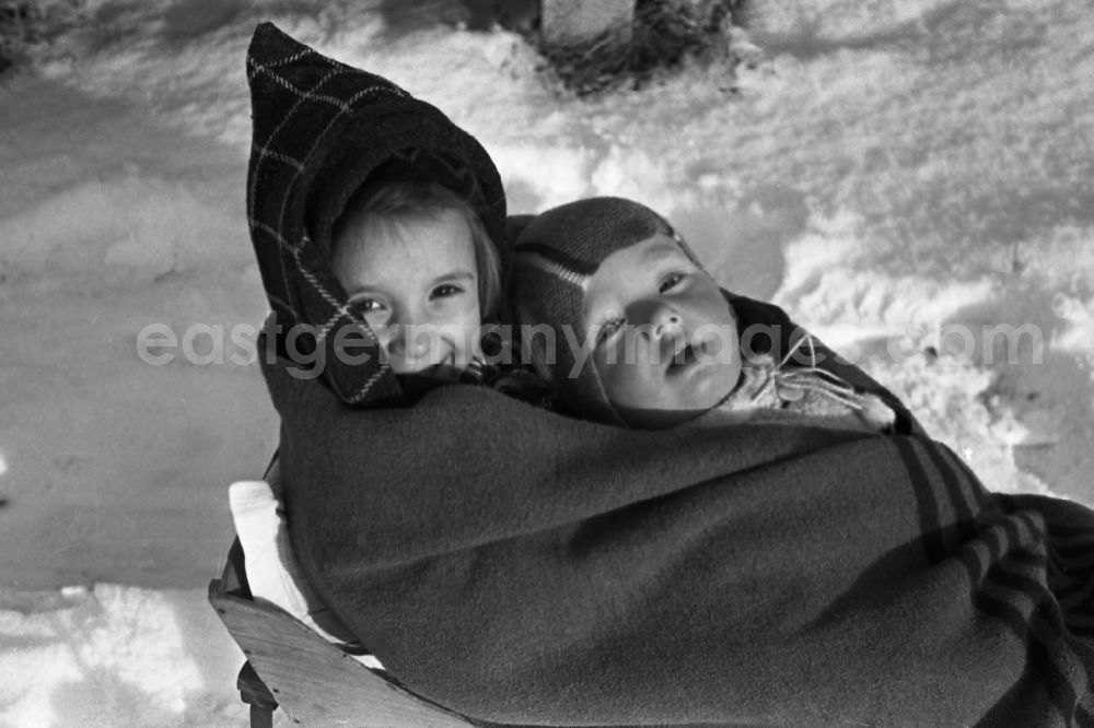 GDR picture archive: Merseburg - Two children lie, muffled in a thick cover, on a sledge in Merseburg in the federal state Saxony-Anhalt in Germany