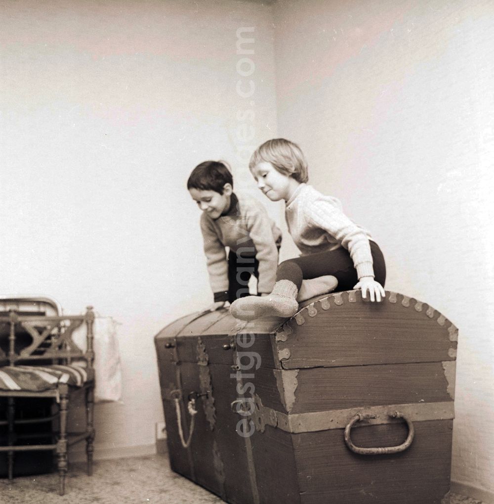 Berlin: Two children sit on a big old wooden chest / wooden box in Berlin, the former capital of the GDR, German democratic republic