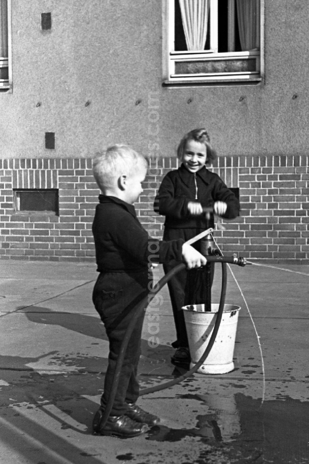GDR picture archive: Merseburg - Two children play in the inner courtyard with a water hose in Merseburg in the federal state Saxony-Anhalt in Germany