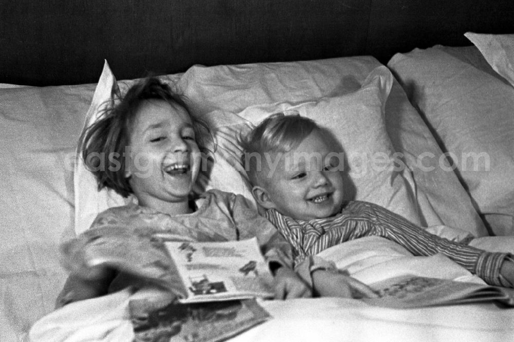 GDR image archive: Merseburg - Two small children lie laughing in the bed of the parents and look to themselves children's books in in Merseburg in the federal state Saxony-Anhalt in Germany