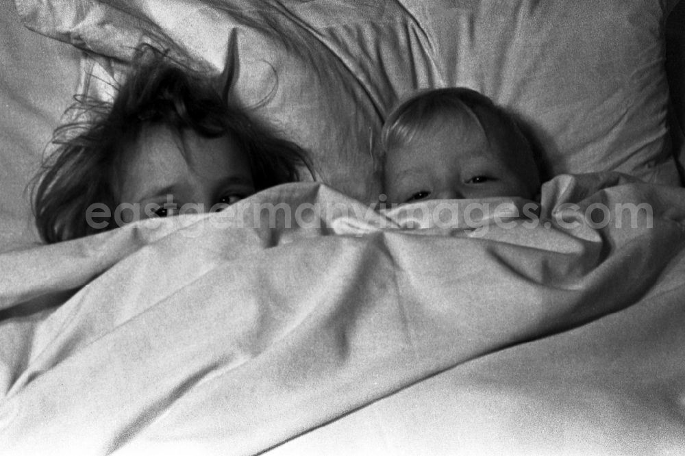GDR photo archive: Merseburg - Two small children lie laughing in the bed of the parents and look to themselves children's books in in Merseburg in the federal state Saxony-Anhalt in Germany