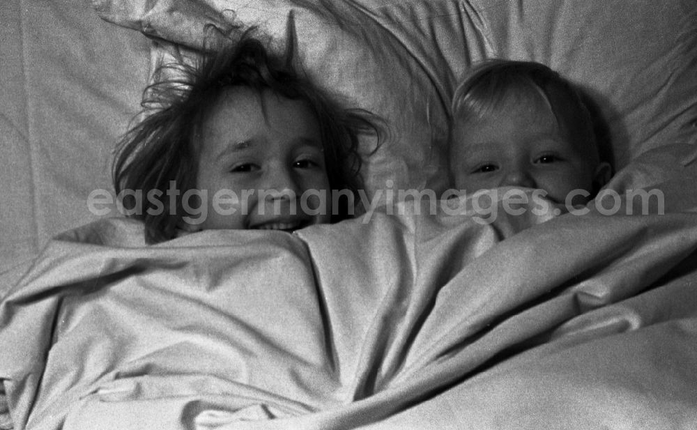 GDR picture archive: Merseburg - Two small children lie laughing in the bed of the parents and look to themselves children's books in in Merseburg in the federal state Saxony-Anhalt in Germany