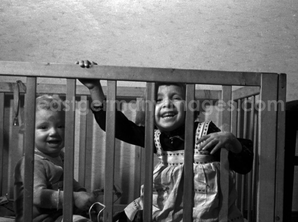 GDR picture archive: Merseburg - The big sister plays with her smaller brother in the playpen in Merseburg in the federal state Saxony-Anhalt in Germany