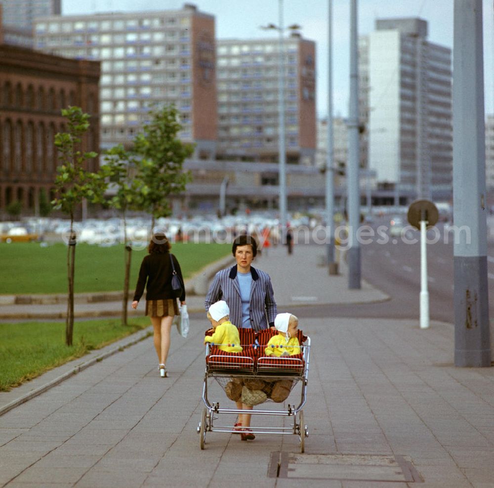 GDR photo archive: Berlin - Eine Mutter schiebt einen Zwillingskinderwagen mit ihren beiden kleinen Kindern nach Hause, das Netz des Kinderwagens ist voll gefüllt mit Tüten vom Einkauf. Im Hintergrund das Rote Rathaus und die Rathauspassagen.