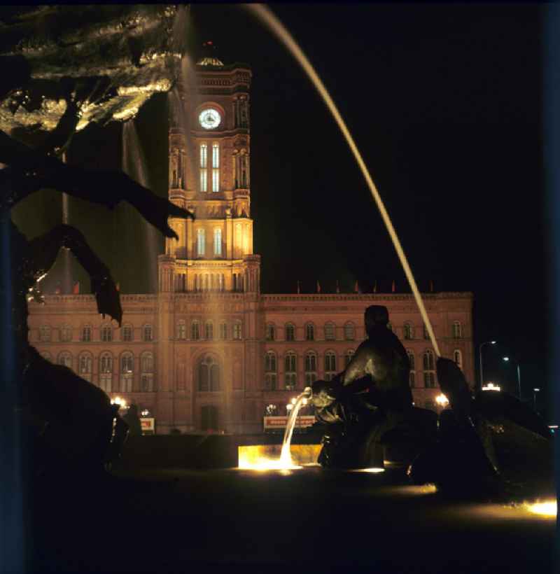Nachtaufnahme: Blick durch die Wasserfontänen des Neptunbrunnens auf das Rote Rathaus in Berlin-Mitte am Jahrestag der DDR. Mit der Errichtung des Fernsehturms sowie der Umgestaltung seiner Umgebung Mitte der 6