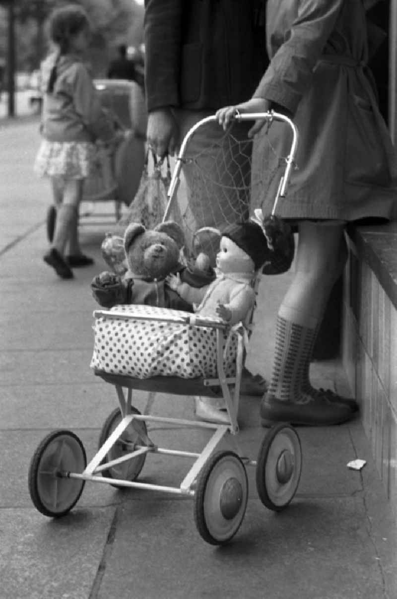 Ein Mädchen schaut neugierig durch das Schaufenster eines Dresdner Spielwarengeschäftes, in der Hand ihren Puppenwagen mit Teddy und Püppi.