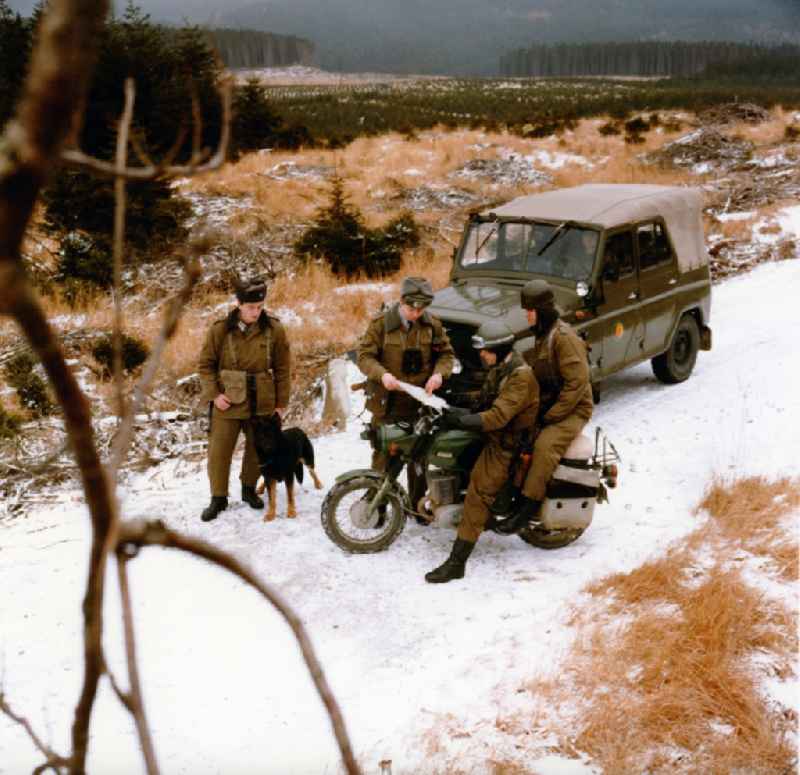 Border Patrol in snow in the winter with dog, car and motorcycle near Abbenrode in today's federal state of Saxony-Anhalt. The border guards are equipped with AK-47 machine guns
