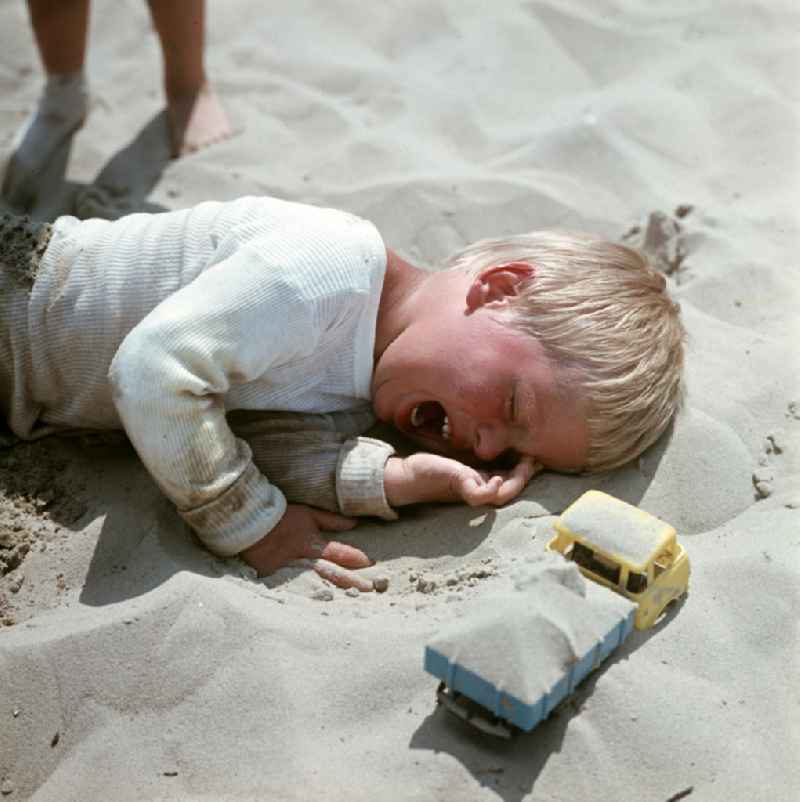 Ein Junge liegt weinend im Sand am Ostseestrand bei Ahlbeck auf der Insel Usedom.