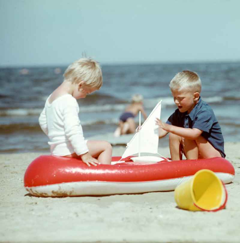 Zwei Jungs sitzen in einem Schlauchboot am Ostseestrand bei Ahlbeck auf der Insel Usedom und spielen mit einem kleinen Segelschiff.