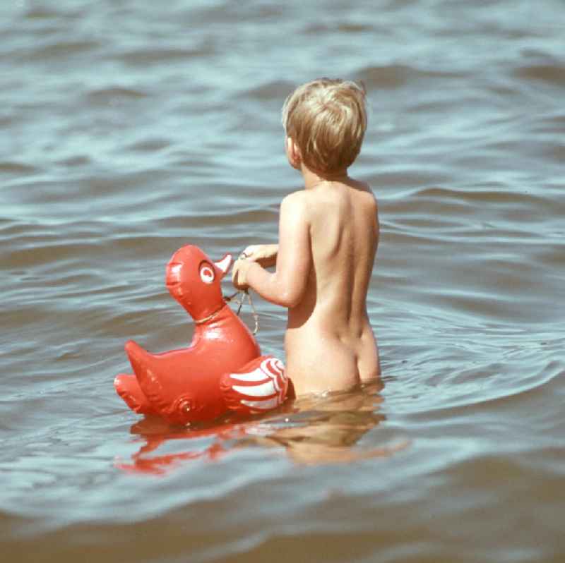 Ein kleiner Junge geht zögerlich mit seiner Schwimmente ins Wasser der Ostsee bei Ahlbeck auf der Insel Usedom.