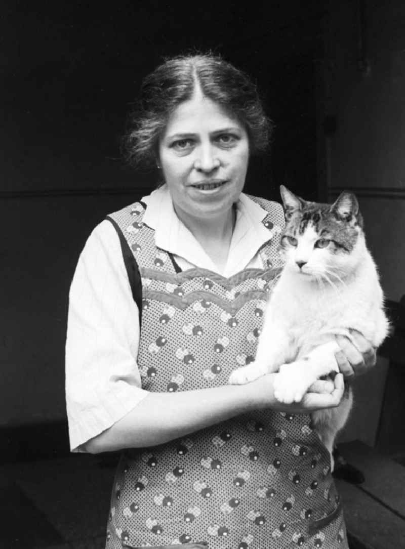 A woman with striking features and smock apron holds a cat on the arm in Arnstadt in the federal state Thuringia in the area of the former GDR, German democratic republic