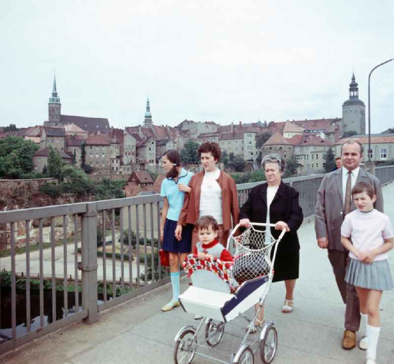 Ein Familie spaziert über die Friedensbrücke in Bautzen. Im Hintergrund sieht man die Altstadt von Bautzen mit Resten der Stadtmauer. V.l.n.r. der Turm des Dom St. Petri zu Bautzen, der Turm des Rathauses und der Lauenturm.