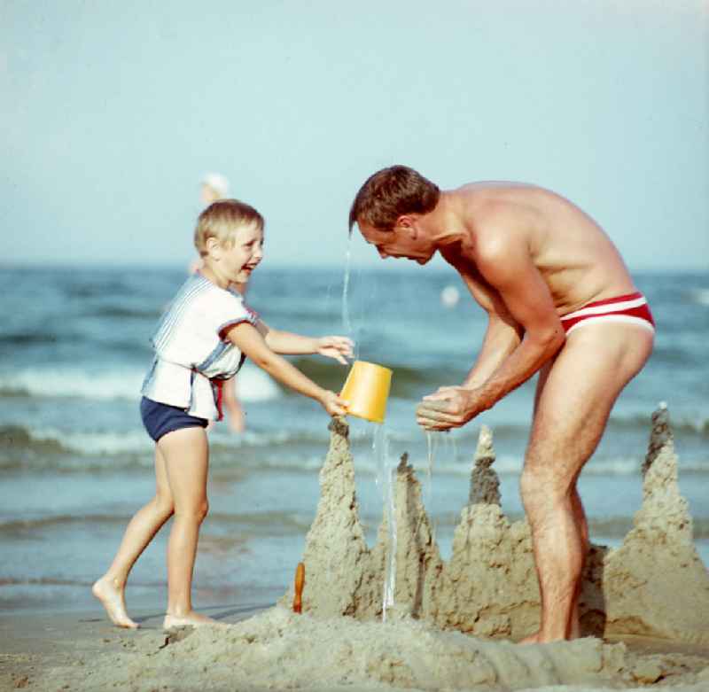Vati und Kind bauen eine Kleckerburg am Sandstrand an der Ostsee bei Bergen auf Rügen.