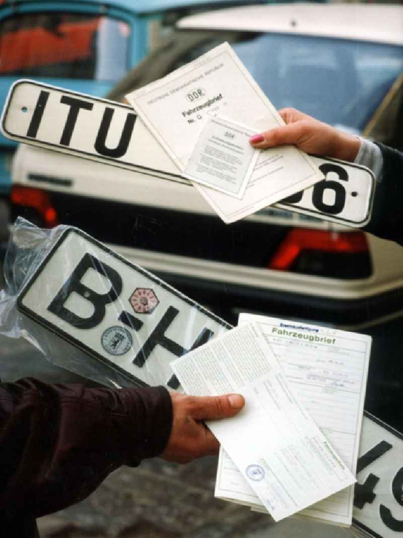 Umstellung der Autokennzeichen, alle Berliner Autos fahren bald nur mit dem Kennzeichen 'B'. Hände halten DDR-Autokennzeichen, BRD-Autokennzeichen sowie jeweilige Autopapiere.