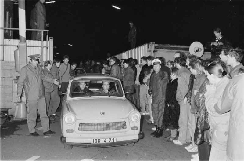 Grenzöffnung am ehemaligen Grenzübergang Invalidenstrasse in Mitte. Auto vom Typ Trabant überquert durch ein Tor die Grenze der DDR nach West-Berlin, drumherum stehen Schaulustige und Polizisten.