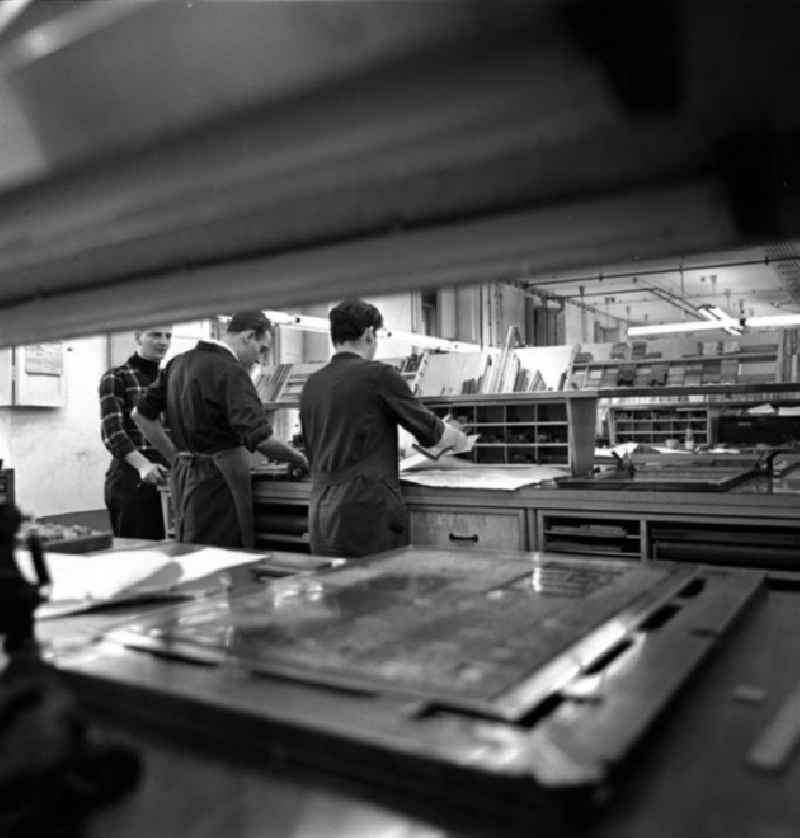 Blick durch einen Werktische mit Druckplatte in der Setzerei vom Neuen Deutschland (ND) auf Arbeiter an der Werkbank.