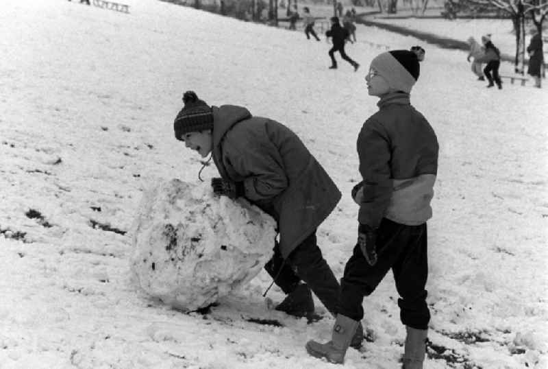 Zwei Kinder formen Schneekugeln im Volkspark Friedrichshain, um einen Schneemann zu bauen.