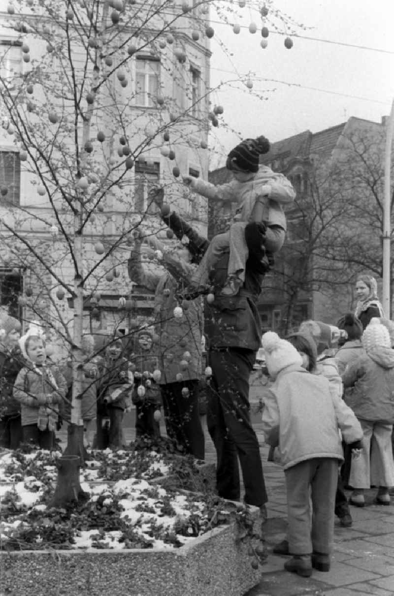 In Berlin-Pankow, children and their parents decorate an Easter tree with self-painted Easter eggs on a pedestrian boulevard