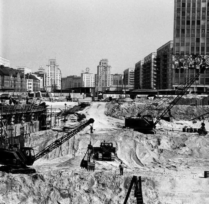 Eine Großbaustelle mit Baumaschinen am Alexanderplatz mit Blick auf fertiggestellte Neubauten in der Karl-Marx-Allee. Rechts ist das Haus des Lehrers mit dem Wandrelief zu sehen, daneben entsteht die Kongreßhalle.
