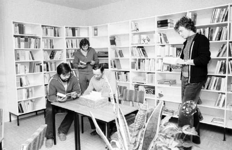 Blick in die Bibliothek / Freizeitraum des Arbeiterwohnheim an der Rhinstraße / Ecke Landsberger Allee, dem heutigen COMFORT Hotel. Männer sitzen am Tisch bzw. stehen und lesen.