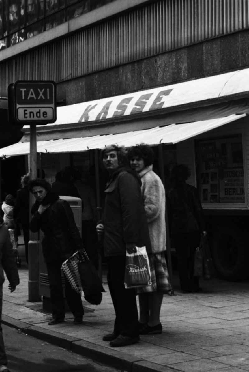 Unweit eines Kassenwagen für den Zirkus Busch warten Menschen am S-Bahnhof Alexanderplatz in Berlin auf ein Taxi am Taxistand. Das kostet vor allem Zeit. Taxen sind auf den DDR-Straßen rar, deshalb verdienen sich auch viele private PKW-Besitzer mehr oder weniger geduldet als Schwarztaxi noch Geld hinzu.