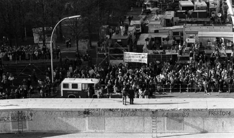 Tausend Neugierige und Pressevertreter haben sich auf der Westseite der Berliner Mauer am Brandenburger Tor versammelt. Am 9. November ist das Bauwerk durchlässig geworden, nachdem SED-Politbüromitglied Günter Schabowksi in einer vom Fernsehen direkt übertragenen Pressekonferenz gesagt hatte: '... haben wir uns dazu entschlossen, heute eine Regelung zu treffen, die es jedem Bürger der DDR möglich macht, über Grenzübergangspunkte der DDR auszureisen.' Das trat ab sofort in Kraft. Resultat war ein sofortiger Ansturm der Massen auf die Übergänge und völlig rat- und hilflose Grenzschützer. Die Mauer am Brandenburger Tor blieb aber noch bis 22. Dezember undurchlässig.