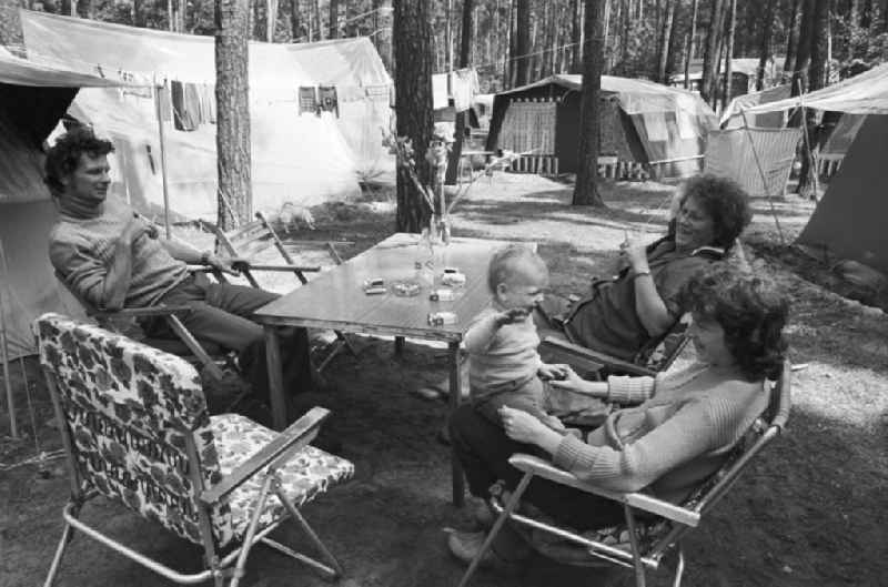 Urlaub auf dem Campingplatz am Zeuthener See in Berlin-Schmöckwitz. Familie sitzt zusammen am Campingtisch vor aufgebauten Zelten.