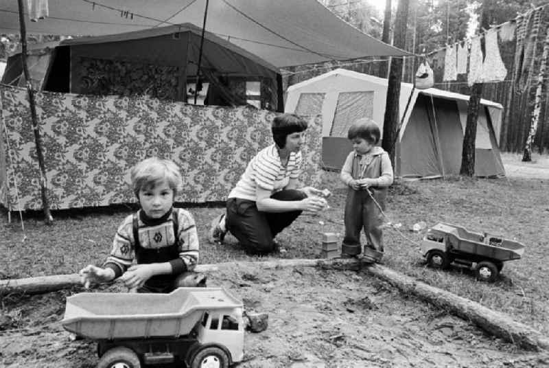 Urlaub auf dem Campingplatz am Zeuthener See in Berlin-Schmöckwitz. Mutter spielt mit ihren Kindern am Sandkasten mit Kipper vor aufgebauten Zelten.
