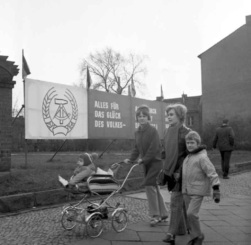 Zwei Mütter mit ihren Kindern laufen an einem Transparent mit Wahlkampfmotiven vorbei. Am 14. November finden die Wahlen zur Volkskammer der DDR und zu den Bezirkstagen statt.