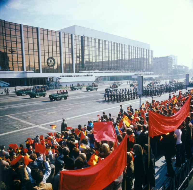 Parade der NVA auf dem Schloßplatz zum 28. Jahrestag der DDR. Soldaten und Schützenfahrzeuge vor dem PdR. Zuschauer mit Winkelementen im Vordergrund. Im Hintergrund der Palast der Republik mit Tribünen. Symbol / Emblem der DDR an der GlasFassade des PdR.