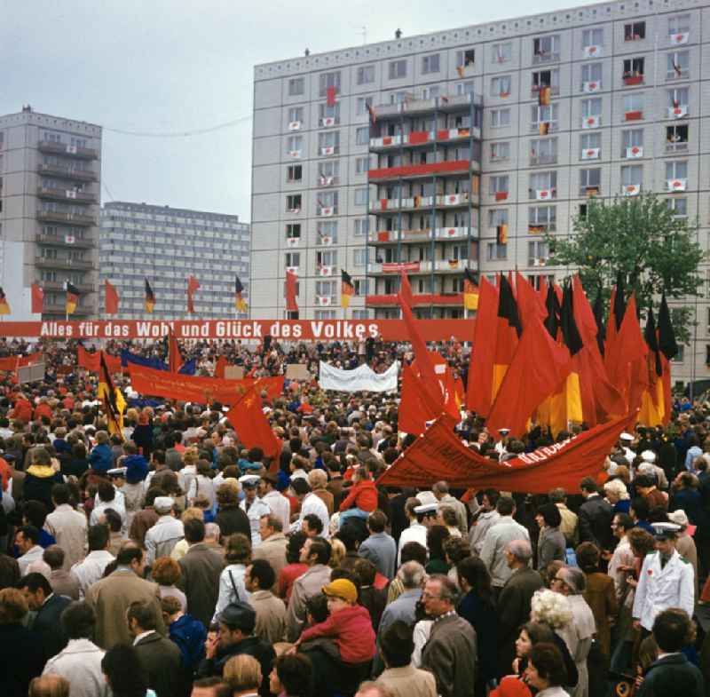 Fahnen und Transparente werden zur traditionellen Demonstration in der Hauptstadt der DDR am 1. Mai 1974, dem 'Internationalen Kampf- und Feiertag der Werktätigen für Frieden und Sozialismus', vor der Ehrentribüne mit der Losung 'Alles für das Wohl und Glück des Volkes' in die Höhe gehalten, aufgenommen auf der Berliner Karl-Marx-Allee.